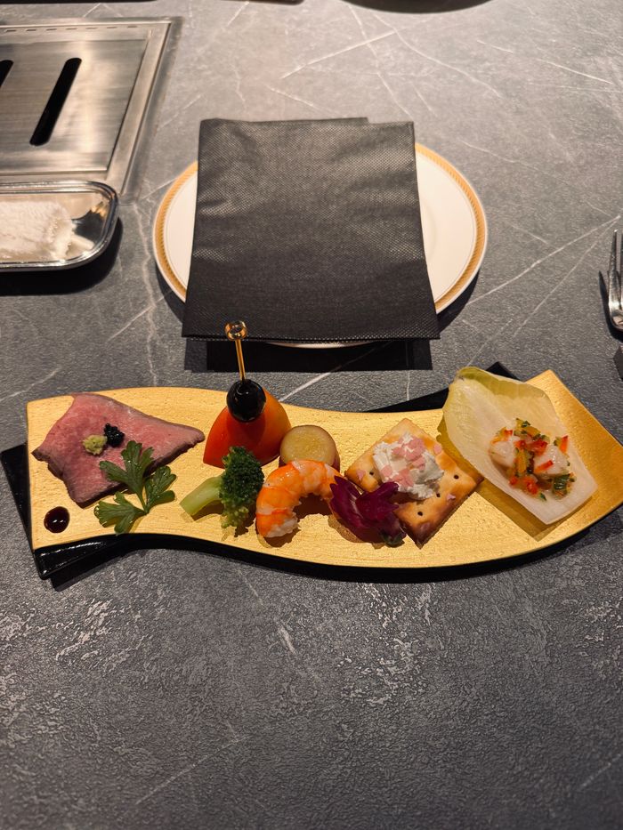 gallery-03 A beautifully arranged gourmet appetizer dish with various delicacies on a gold plate setting.